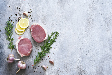 Raw pork steaks on a concrete background with spices and rosemary, top view.