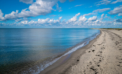 Dramatic cloudscape over the curved beach and the blue sea water with white illuminated reflections