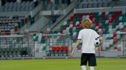 Portarit of Caucasian pre teen kid boy entering the field of huge soccer stadium, holding a ball, dreaming of becoming professional player, soccer star