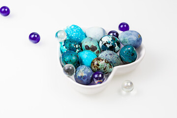 Easter blue quail eggs in a plate in the shape of a heart on a white table