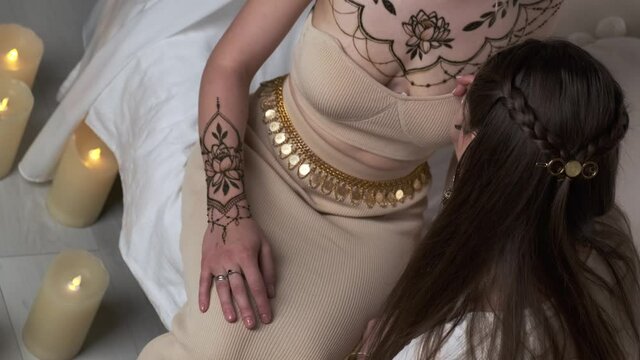 Mehendi artist painting henna tattoo on women chest. Drawing process of henna ornament. Mehndi body art