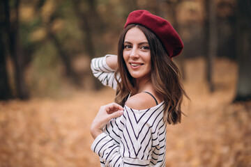 Portrait of brunette woman in autumn in the park. French style. Woman in beret and striped blouse