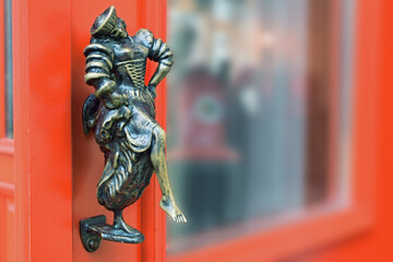 Front door metal decoration. Bronze figurine of a half-naked woman in a medieval costume having fun