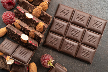 chocolate bars with almonds, raspberries, handmade sweets. Composition of bars and pieces of dark almond chocolate, raspberries on a black background, top view. Pastry craft on the table