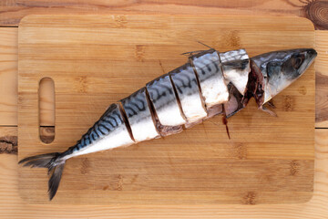 One slightly salted mackerel fish, cut into pieces, on a bamboo cutting board, close-up, top view.