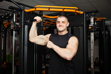 Fototapeta na wymiar young handsome coach in a black uniform against background of a simulator in gym. Muscular athletic body of a bodybuilder, coaching, individual sports and weight loss Portrait. muscles on the arm