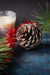primer plano de una piña de piñones con adornos navideños alrededor: espumillón, vela de Navidad y ramas de pino