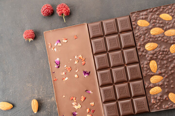 chocolate bars with almonds, raspberries, handmade sweets. Composition of bars and pieces of dark almond chocolate, raspberries on a black background, top view. Pastry craft on the table