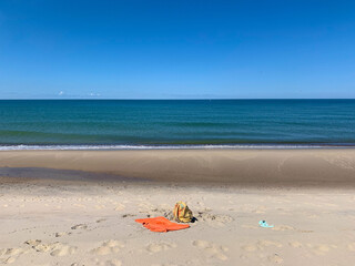 Fototapeta na wymiar Lonely towel on the empty beach, clear blue sky and blue sea