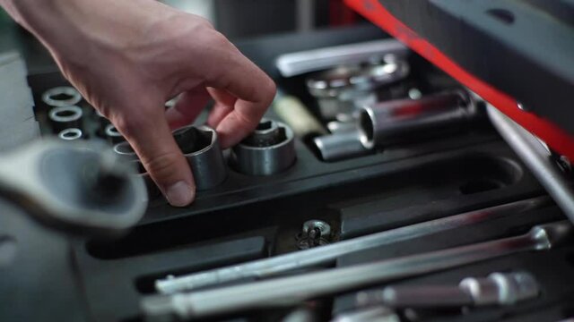 Close-up hands of unrecognizable worker man opening toolbox with auto car tools taking and connecting head socket with tool ratchet wrench spanner. Man picking ratchet wrench from large set.