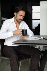 Poranna prasa i praca podczas pierwszej kawy. Przystojny mężczyzna w białej koszuli pije poranną kawę.  - obrazy, fototapety, plakaty