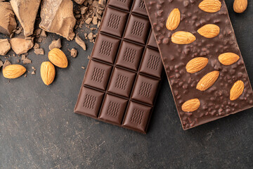 Store Cooking chocolate bars with almonds handmade sweets. Composition of bars and pieces of dark almond chocolate on a black background, top view. Pastry craft on the table
