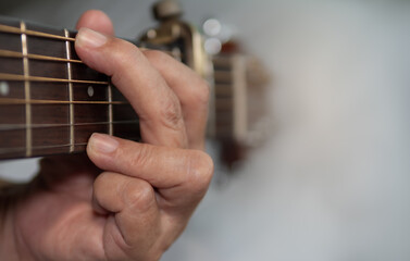 Older woman musician hand holds the neck of classic wooden guitar play G chord. Senior female guitarist put fingers on fingerboard playing G chord song with capo. String musical instrument background.