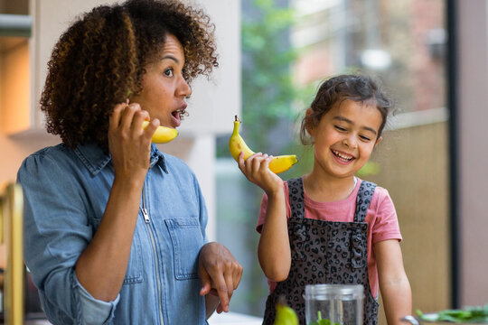 Mixed race girl having fun making a smoothie with mother in kitchen
