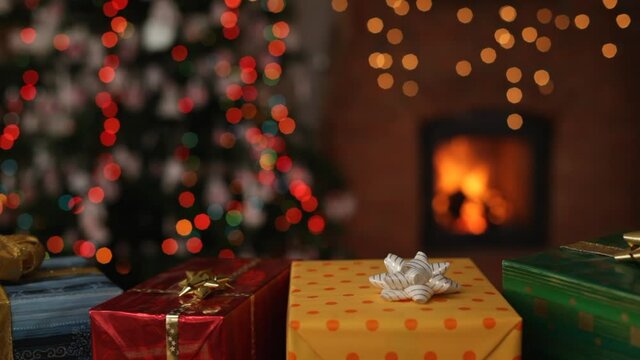 Christmas gifts in front of fireplace and blurry lights on xmas tree in the evening - static camera