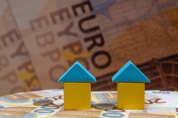 Stylized small conditional yellow-blue houses made of children's cubes against the background of 200 euro bills and a large inscription Euro