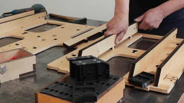 Manufacturing professional die cutter plate - worker hands inserting precision laser cut parts in plywood plank slots using hammer, camera slide