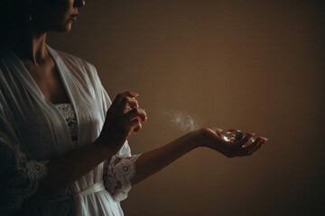 woman in a lacy white robe sprays perfume on her wrist