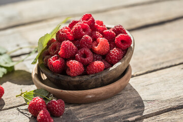 Appetizing juicy ripe raspberries in a bowl surrounded by green raspberry leaves on a wooden ...