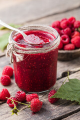 homemade raspberry jam on a wooden background with fresh raspberries, selective focus.