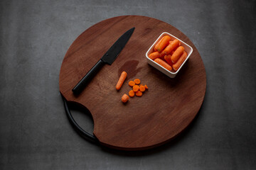 Cut Slices of carrot on a wooden board on dark grey background.