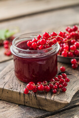 Red, juicy berries of red currants and jars of berry jam on a wooden table