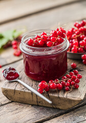 Red, juicy berries of red currants and jars of berry jam on a wooden table