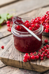 Red, juicy berries of red currants and jars of berry jam on a wooden table