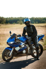 Motorcycle driver in helmet and leather jacket sits on sports motorcycle on the road against forest...
