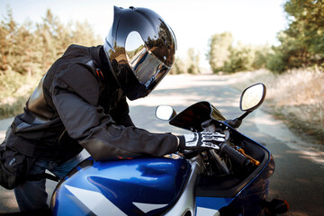 Motorcycle driver in helmet and leather jacket sits on sports motorcycle on the road against forest...