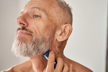 Obraz premium Mature man with naked torso shaving beard with electric razor