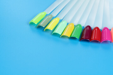 Fototapeta premium Multiсolor nail tips on a blue background. examples of manicure for nails. Palette with color samples of nail. Copy space