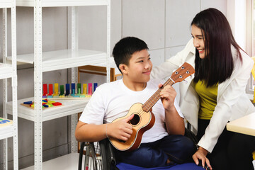 Happy child having fun during study at school, smiling boy sitting in wheelchair learning to play ukulele with teacher, education of kid with physical disability concept.