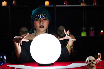Luminous crystal ball and cards on magnificent fortune telling table with mysterious beautiful woman fortune teller in black dress, dark witch try to read future on magical ball. - obrazy, fototapety, plakaty