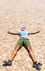 a man lies on dry ground covered with cracks. Tired of the heat man lies in the desert