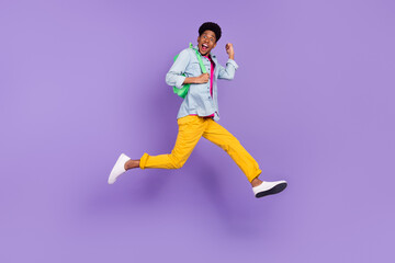 Fototapeta na wymiar Photo of cheerful guy jump hurry run raise fist wear backpack blue shirt isolated purple color background