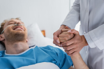 doctor holding hand of blurred and smiling patient with nasal cannula