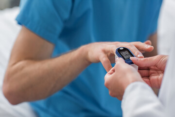 cropped view of doctor placing pulse oximeter on finger on patient in hospital