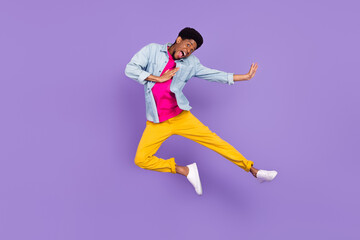 Fototapeta na wymiar Photo of careless funky energetic guy jump kick leg wear blue shirt pants sneakers isolated purple color background