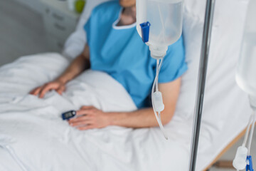 drop counter with intravenous therapy bottle near blurred patient in hospital bed