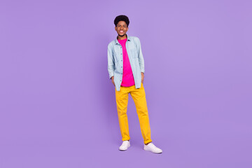 Photo of cute funny dark skin guy dressed jeans shirt arms pockets smiling isolated violet color background