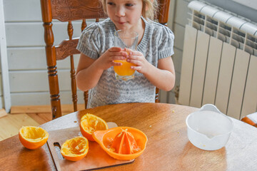 the child girl in the kitchen cuts and squeezes oranges juice