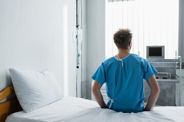 Fototapeta premium back view of curly man sitting on hospital bed