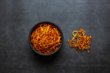 Dried cordyceps militaris mushroom in bowl on dark grey background. Cordyceps flower