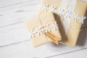 Christmas presents on white wooden background. Natural winter theme decoration, brown paper, twine, snowflake ribbon, tag. Selective focus. Sustainable gift wrapping. Gift giving. Merry Christmas.
