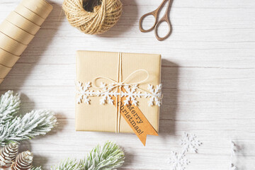 Christmas composition with holiday decoration, present, tree branches, pine cones, twine, natural paper on white wooden background. Holiday craft. Sustainable gift wrapping. Merry Christmas.