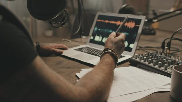 Mid-section tracking of unrecognizable man sitting at table and talking into microphone while recording podcast