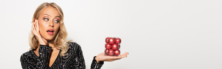 astonished and elegant woman with set of christmas balls isolated on white, banner