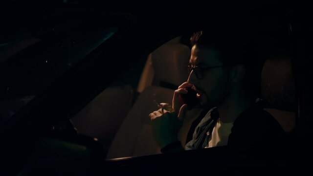 European man talks aggressively on the phone and smokes a cigarette in the car at night