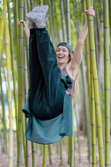 Laughing hip-hop girl hung with her legs lifted up on green trunks in a bamboo grove